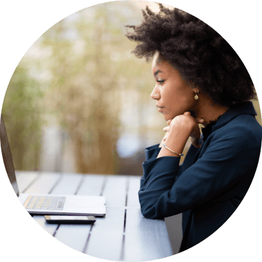 Woman with Afro Hair and Navy Shirt looking at Laptop on Table